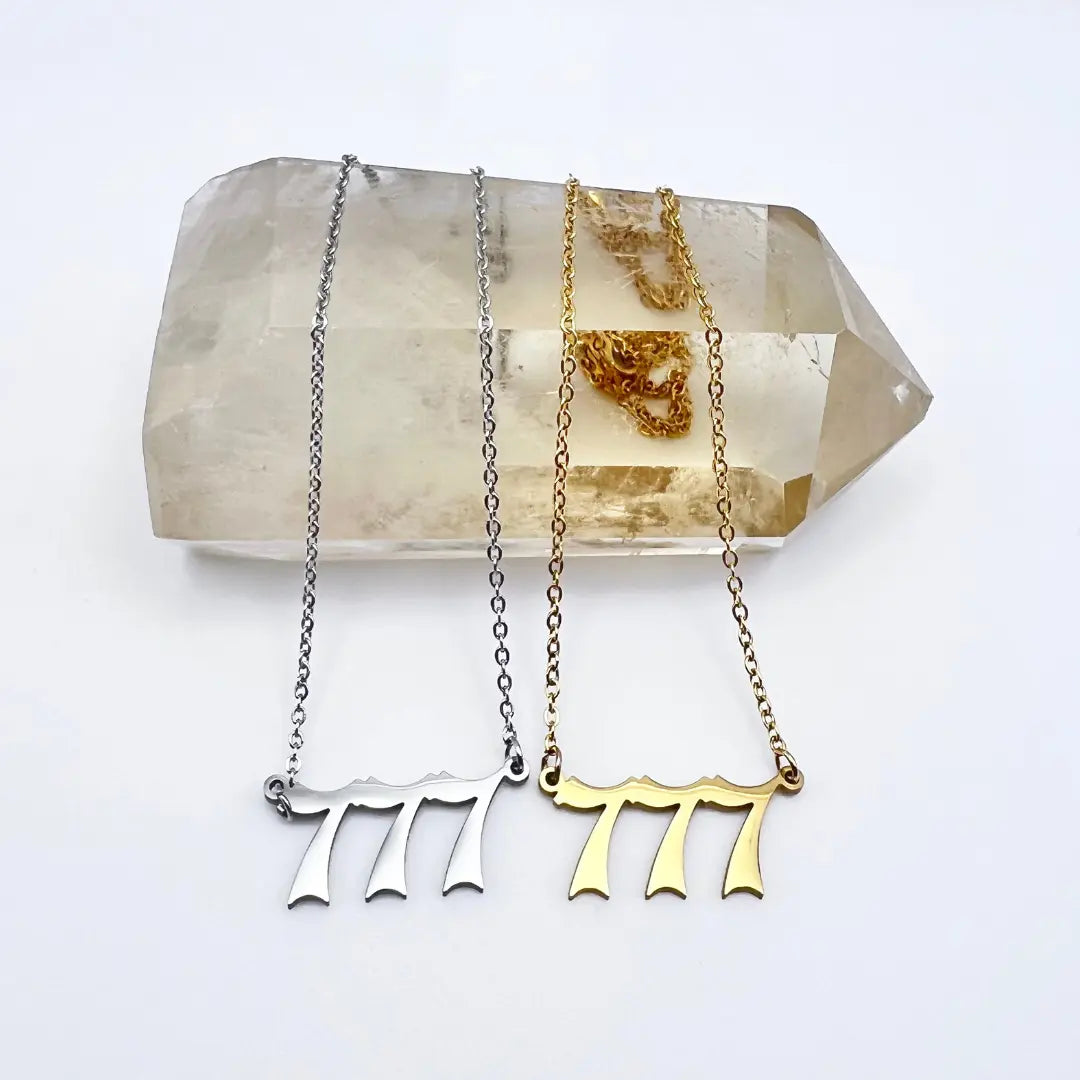 Displayed on a large, clear crystal are two necklaces from Ascention Beauty, the Angel Number Necklaces. One in silver and the other in gold, these pieces rest elegantly against the crystal's surface, embodying angelic messages and spiritual guidance with their divine elegance.