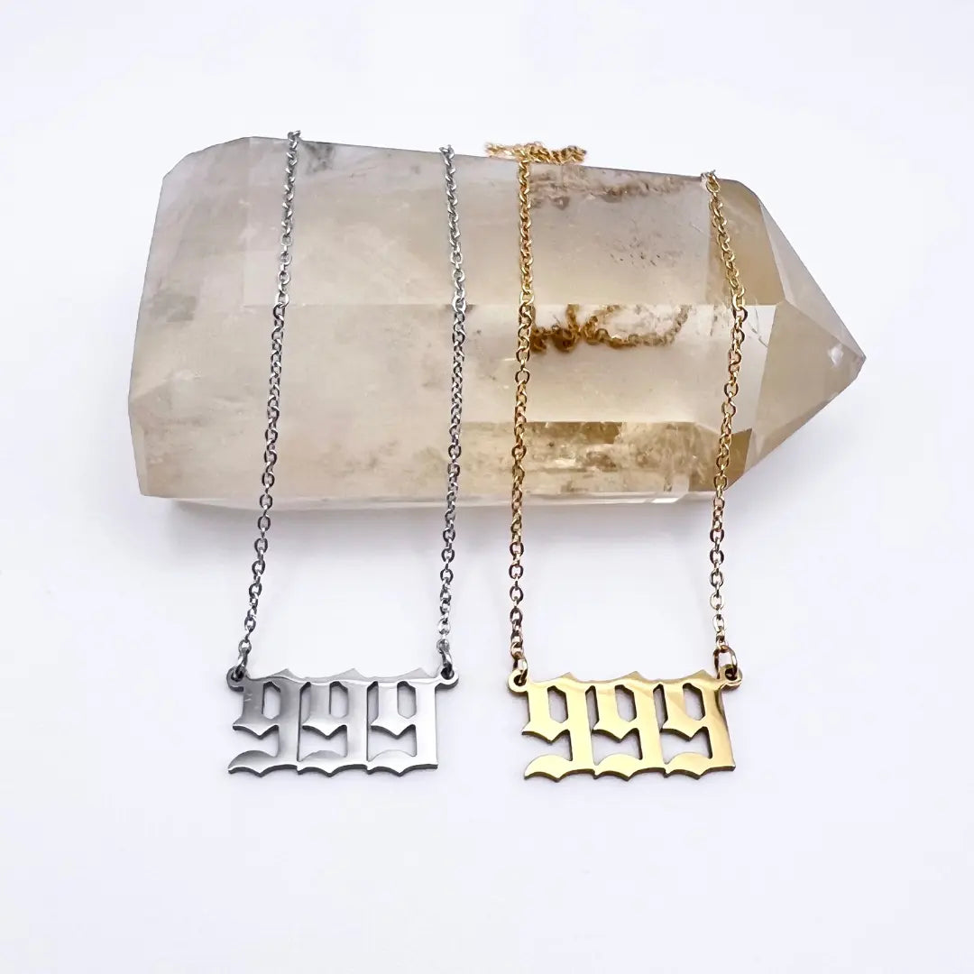 The Angel Number Necklaces from Ascention Beauty rest gracefully on a large, clear crystal, with numbers boldly crafted in an old-style font. One silver and one gold, these necklaces symbolize divine guidance, serving as elegant reminders of angel messages and spiritual guides.